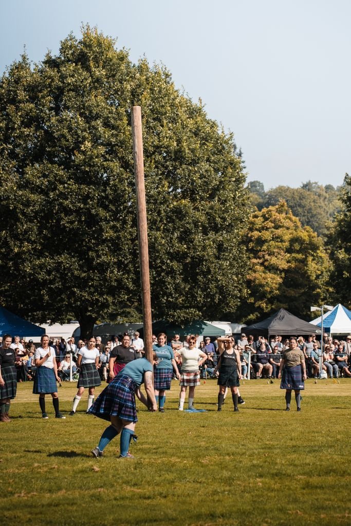 Participants compete in the traditional caber toss at the Scottish Highland Games in a lush outdoor setting.