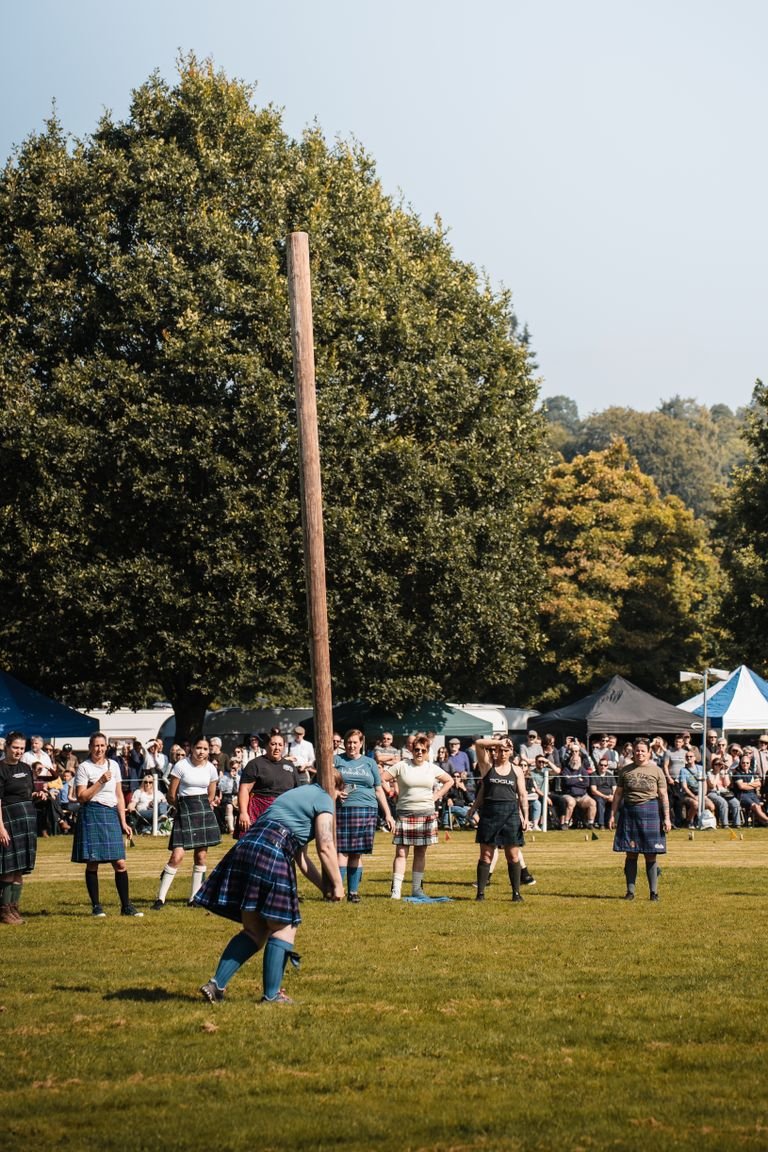 Participants compete in the traditional caber toss at the Scottish Highland Games in a lush outdoor setting.