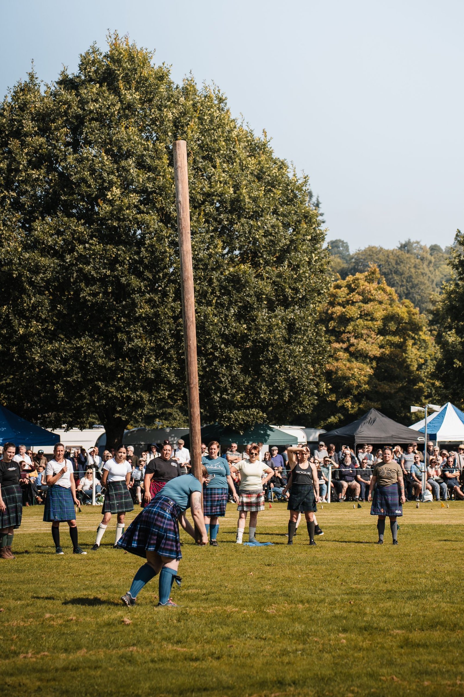 Participants compete in the traditional caber toss at the Scottish Highland Games in a lush outdoor setting.